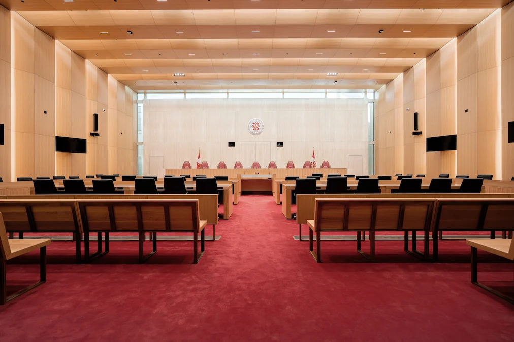 La salle d’audience principale de la Cour suprême du Canada dans l’Édifice commémoratif de l’Ouest. Le plafond et les murs comprennent des arches en bois séparées par des puits de lumière et le tapis est rouge. Le banc des juges se trouve à l’avant de la pièce.