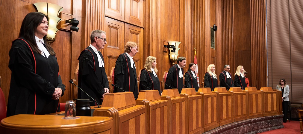 The judges of the Supreme Court of Canada standing behind the bench, wearing ceremonial robes