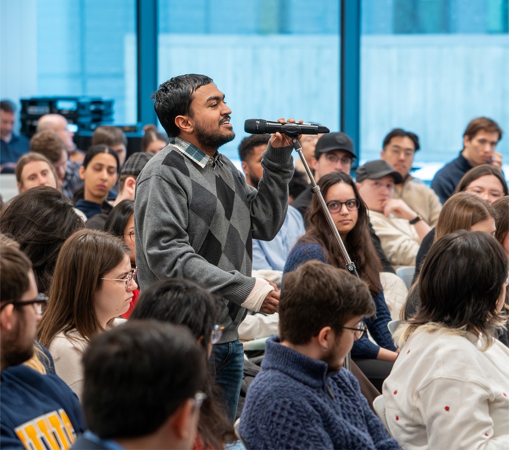 A student speaks at a microphone among audience members