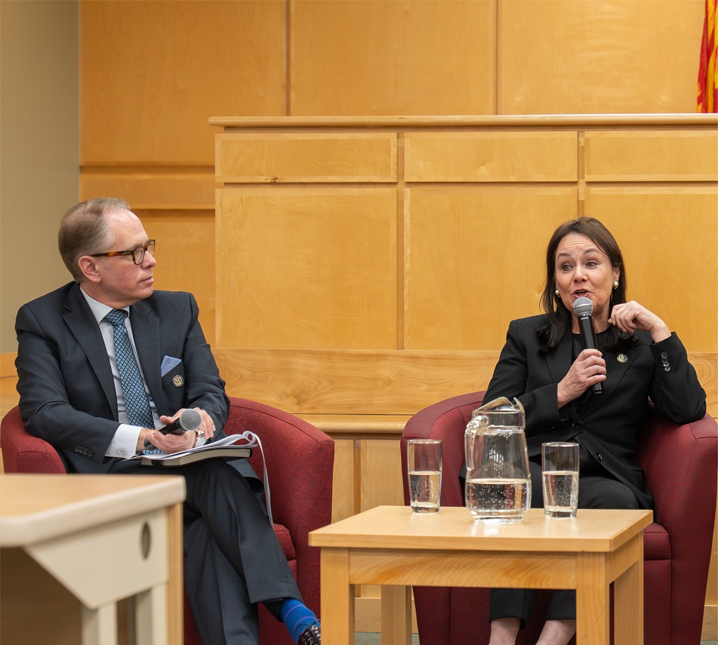Justice Côté speaks into a microphone while a moderator listens