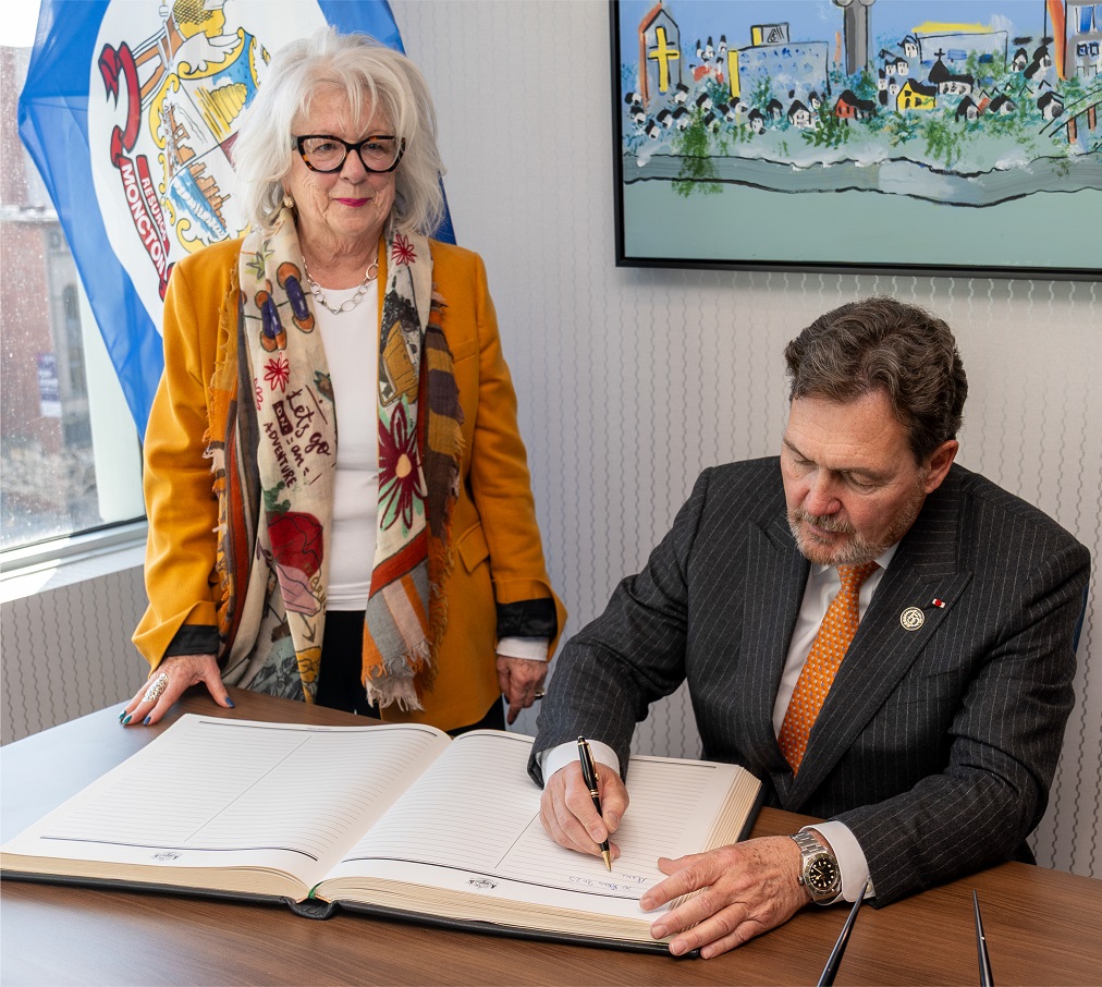 Chief Justice Wagner signs a book while the acting Mayor of Moncton looks on