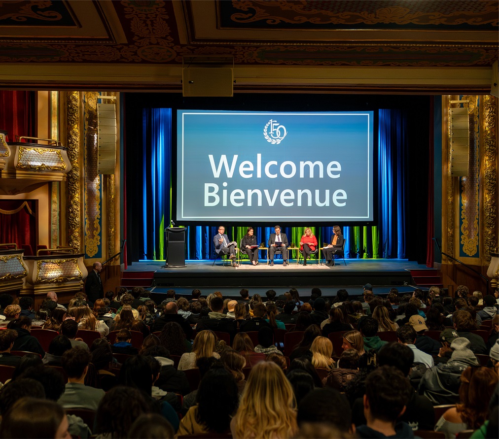 The judges sitting on a stage in front of a large audience