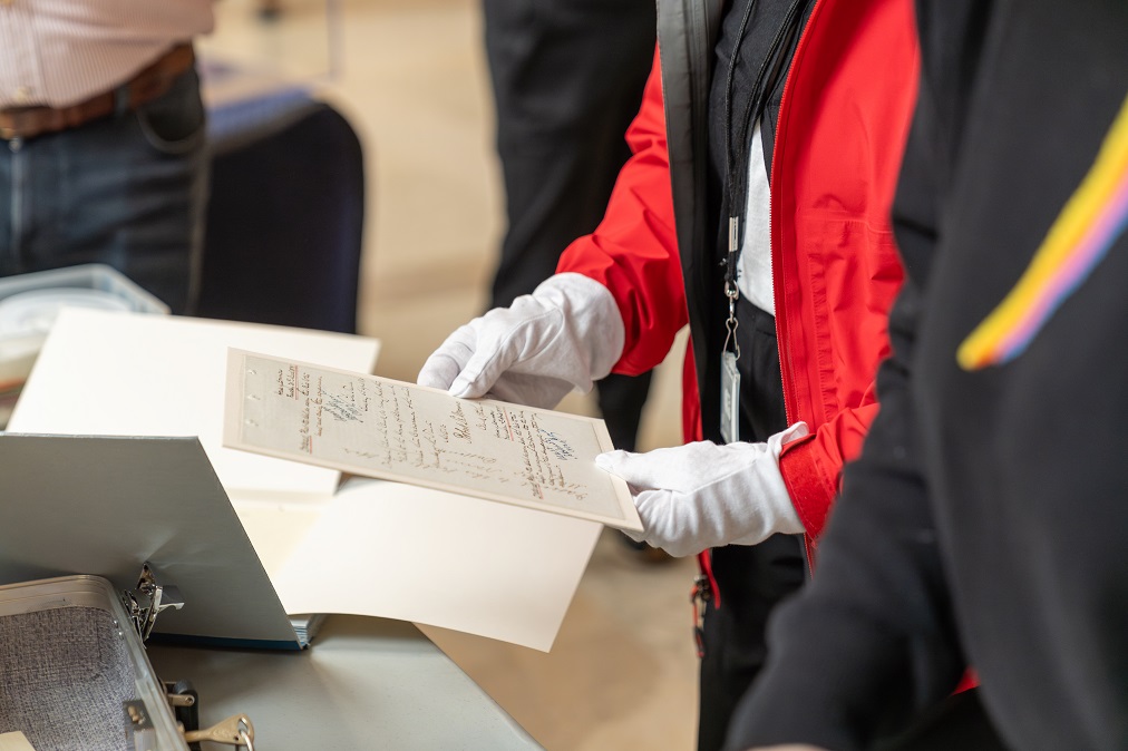 A person wearing white gloves handles archival documents