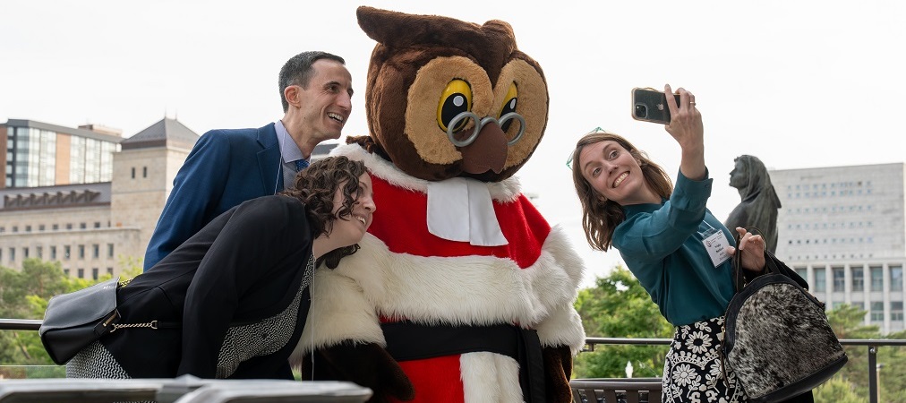 3 people pose for a selfie with Amicus, the mascot of the Supreme Court