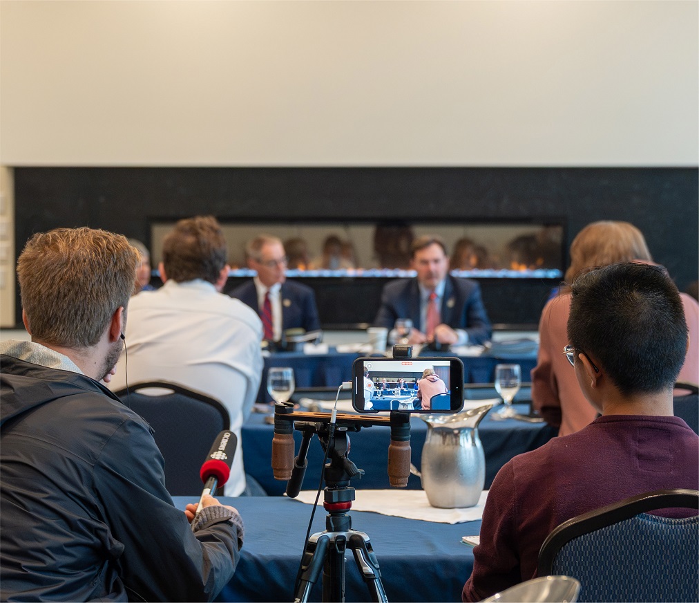 Journalists sit in a meeting room while the judges speak in the background