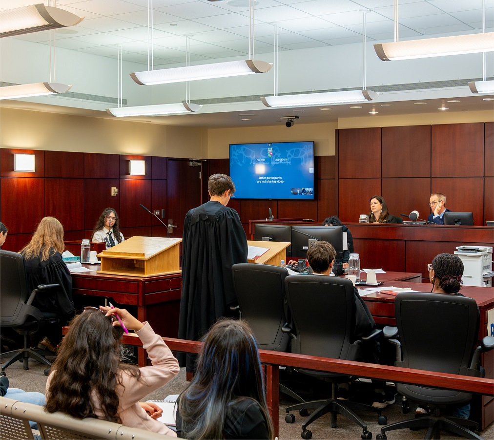 Students in black lawyers’ robes in a courtroom with the judges sitting at the bench