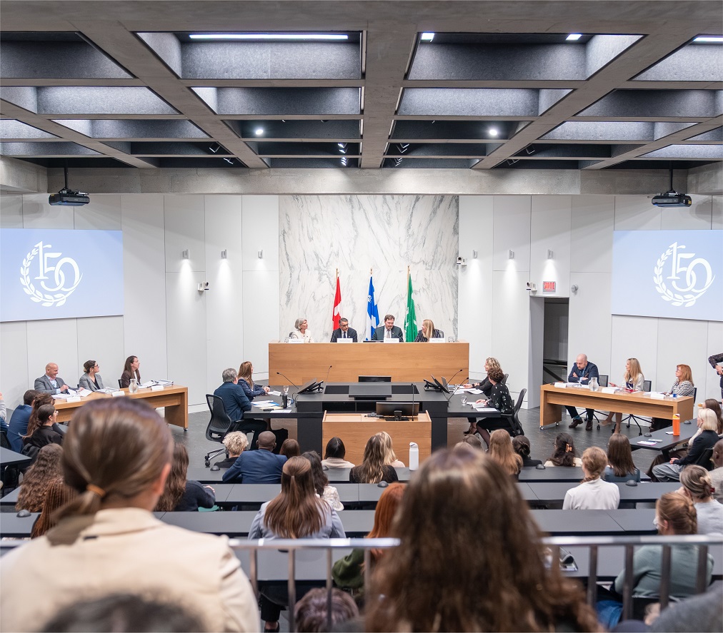 The judges sit on a raised dais in front of an audience in a large auditorium