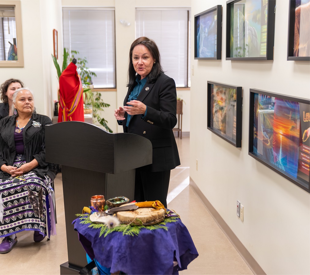 Justice Côté speaks podium while a woman in a ribbon skirt listens